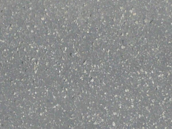 Road edge texture, with grey asphalt embedded with white rocks meeting edges of black-flecked snow, grey sidewalk and a white snow with grey patches.